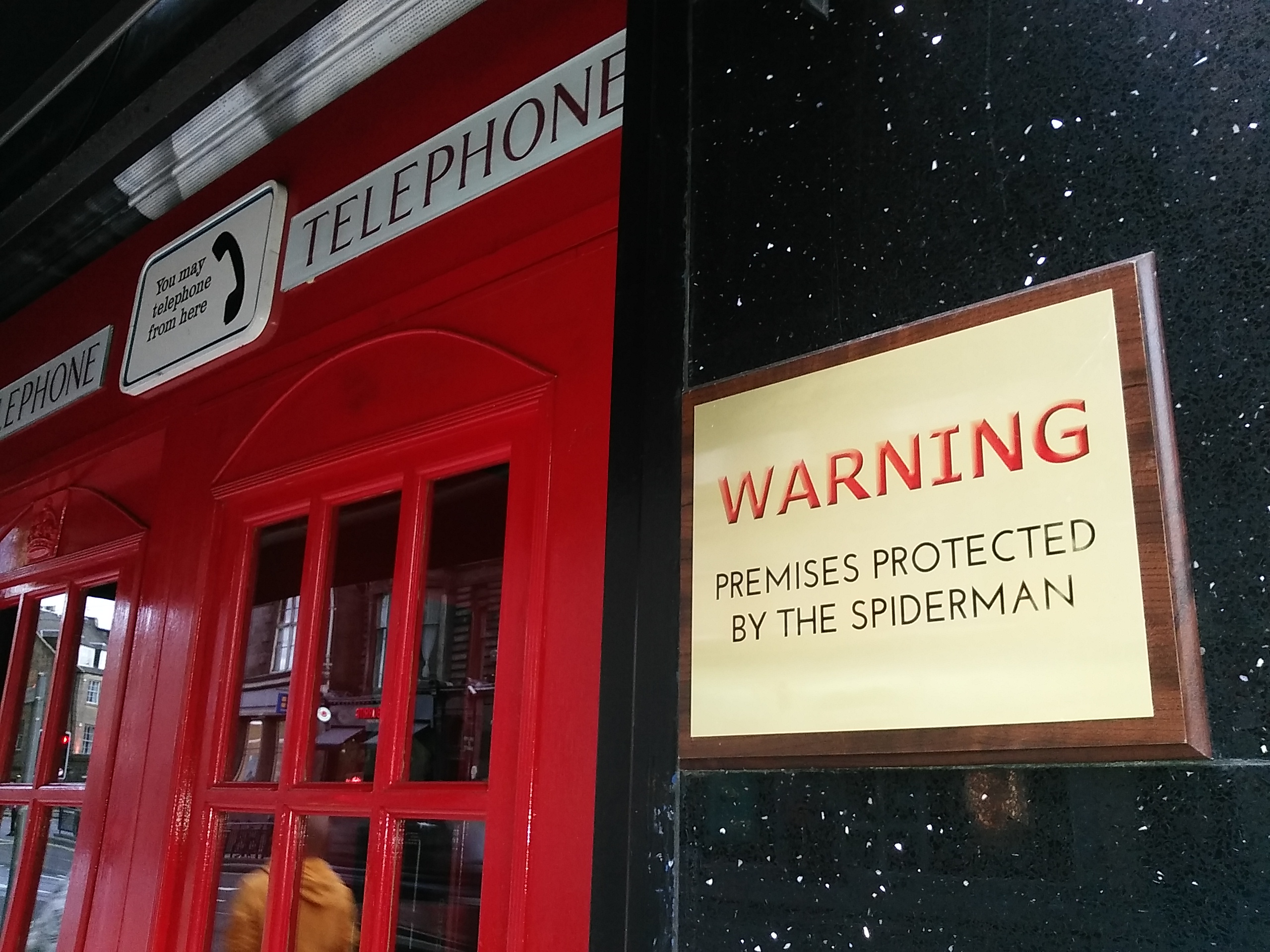 A red telephone cabin guarded by Spiderman