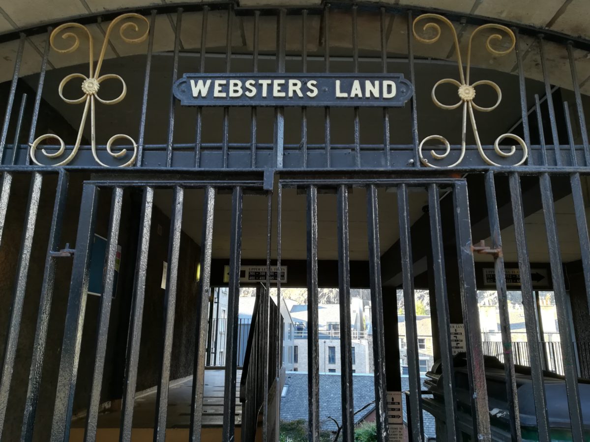 An entrance to a building with a black fence and the title "Websters Land"